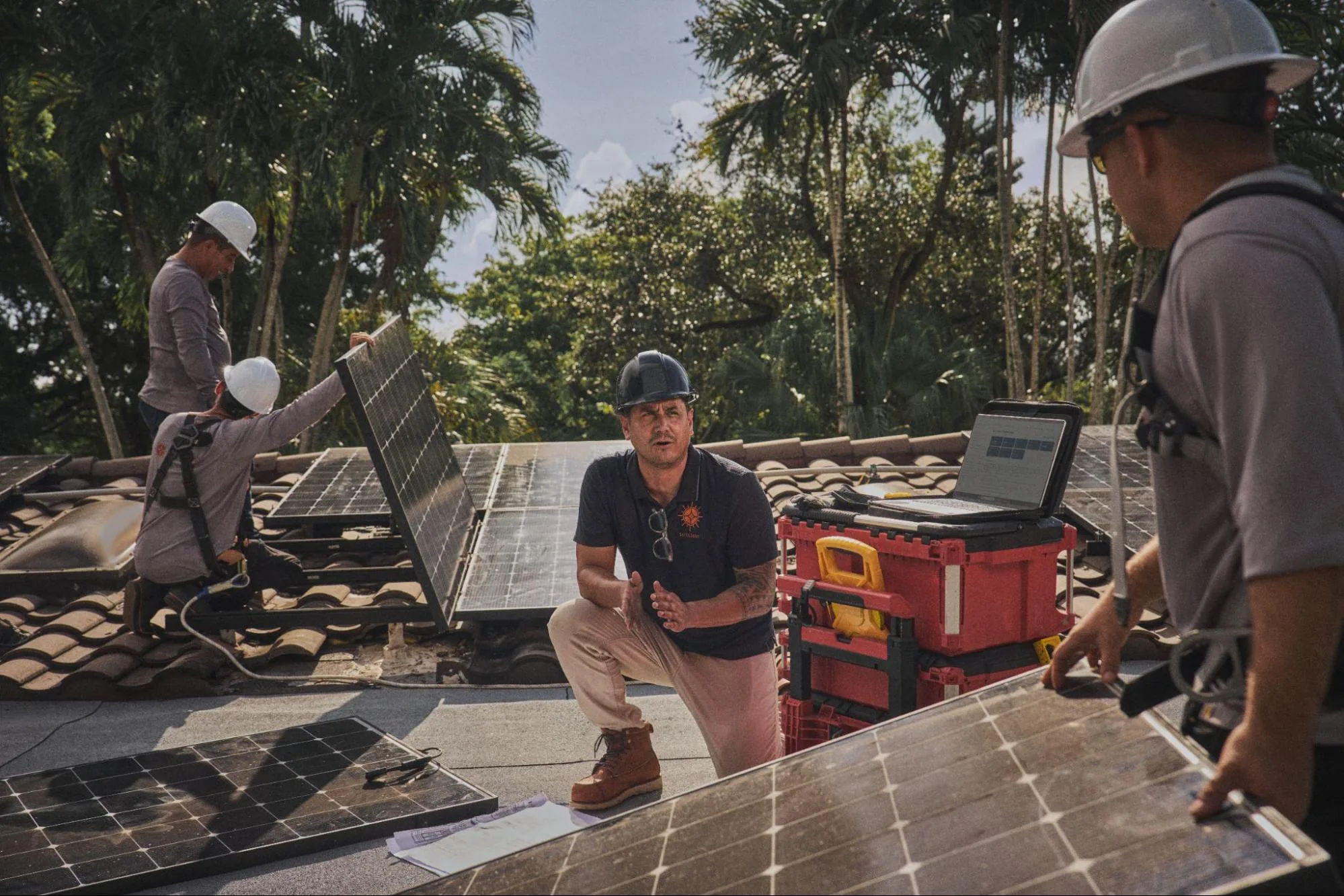 SolarSync crew on a tile roof in South Florida, lifting solar panels while a lead tech kneels beside a red tool case